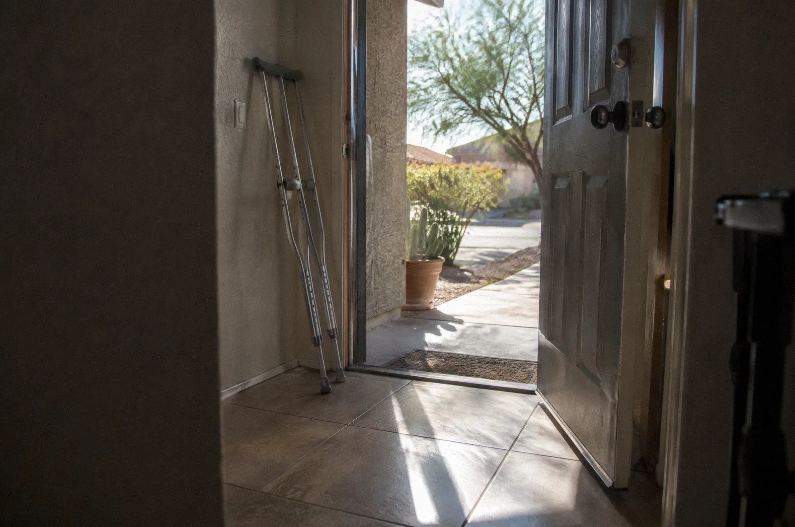 Crutches leaning by a front door of an Arizona home, sunlight across the tile floor